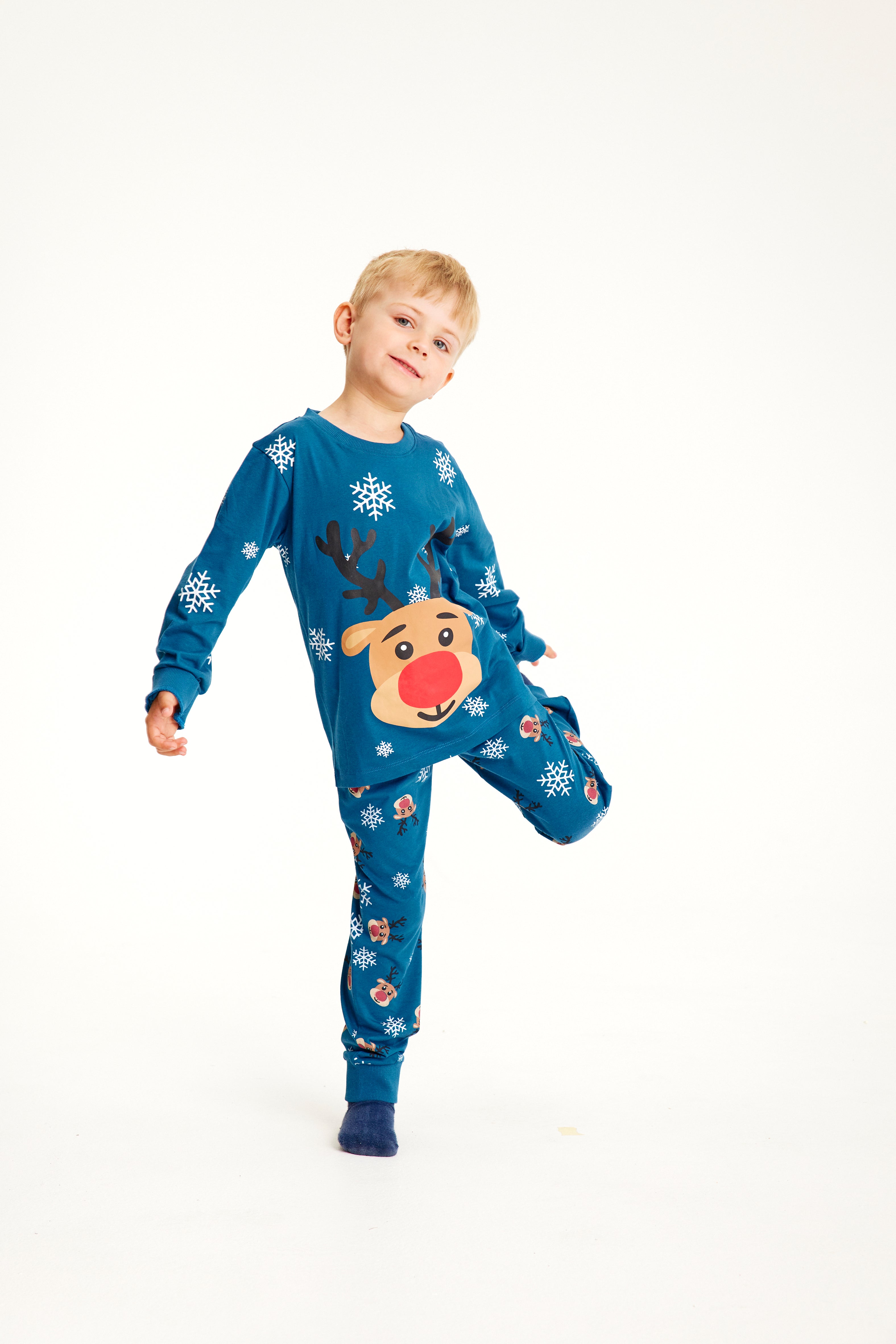 Et barn på ett ben i blå julepyjamas med reinsdyr og snøfnugg.